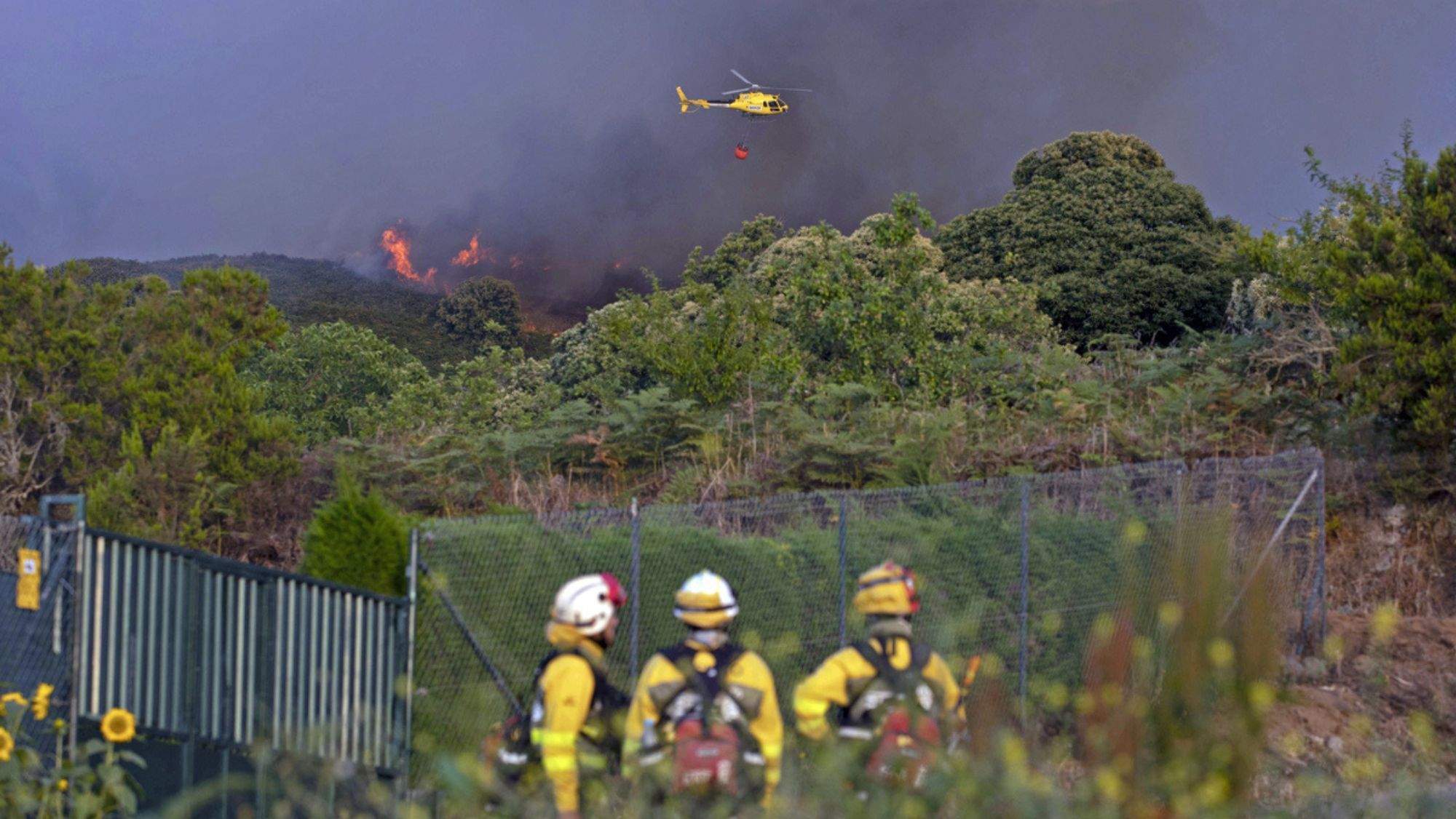 Un helicóptero trabaja en la extinción del incendio ante la atenta mirada de efectivos terrestres. / EFE