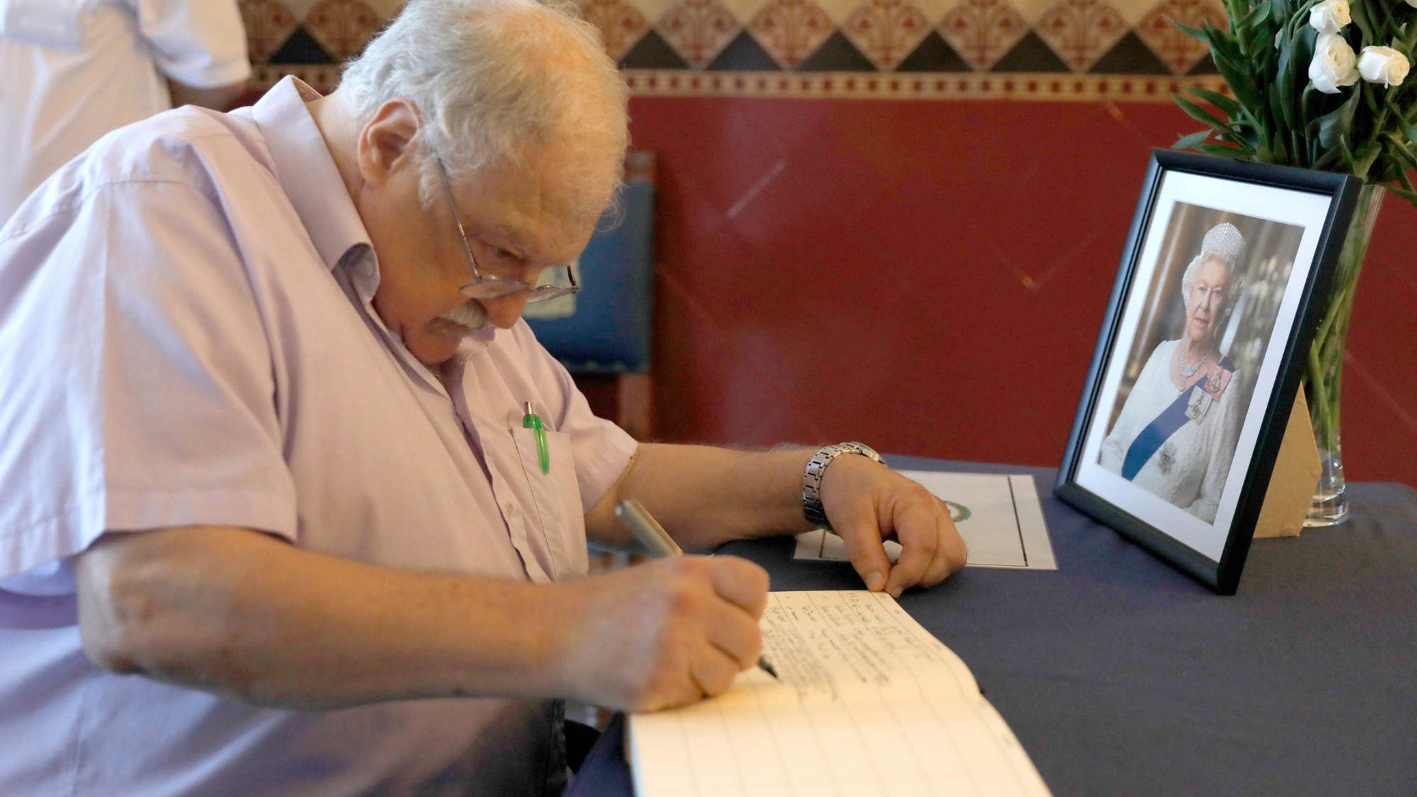 Un hombre escribe sus condolencias por la muerte de la reina Isabel II en el libro dispuesto en la entrada de la Casa del Gobernador de Gibraltar. / EFE