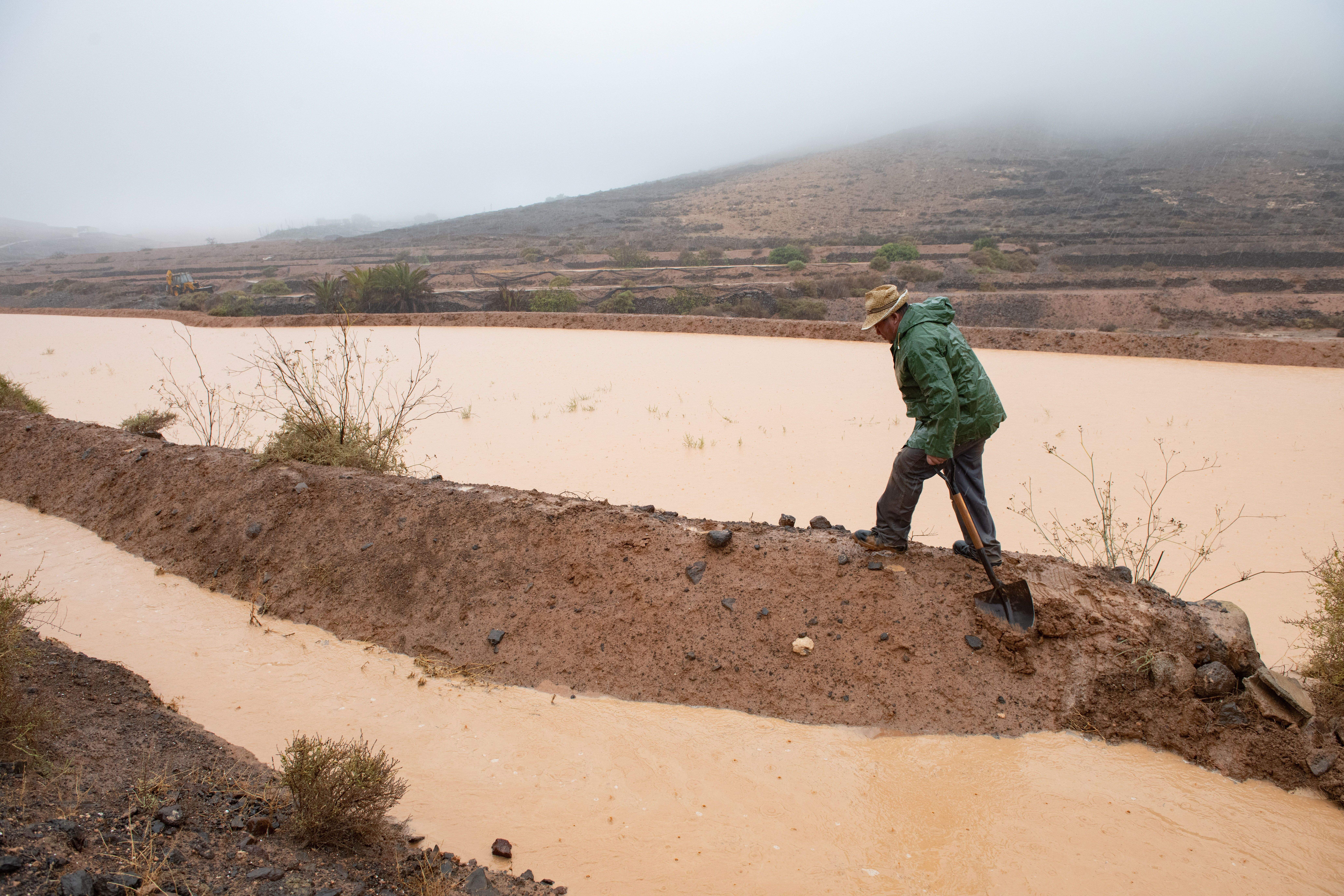 Vecinos del barrio Guisguey en el termino municipal de Puerto del Rosario trabajan en la gavias para tratar de llenarlas aprovechando la lluvia recibida del paso de la tormenta tropical Hermine cerca de Canarias. / Carlos de Saá (EFE)