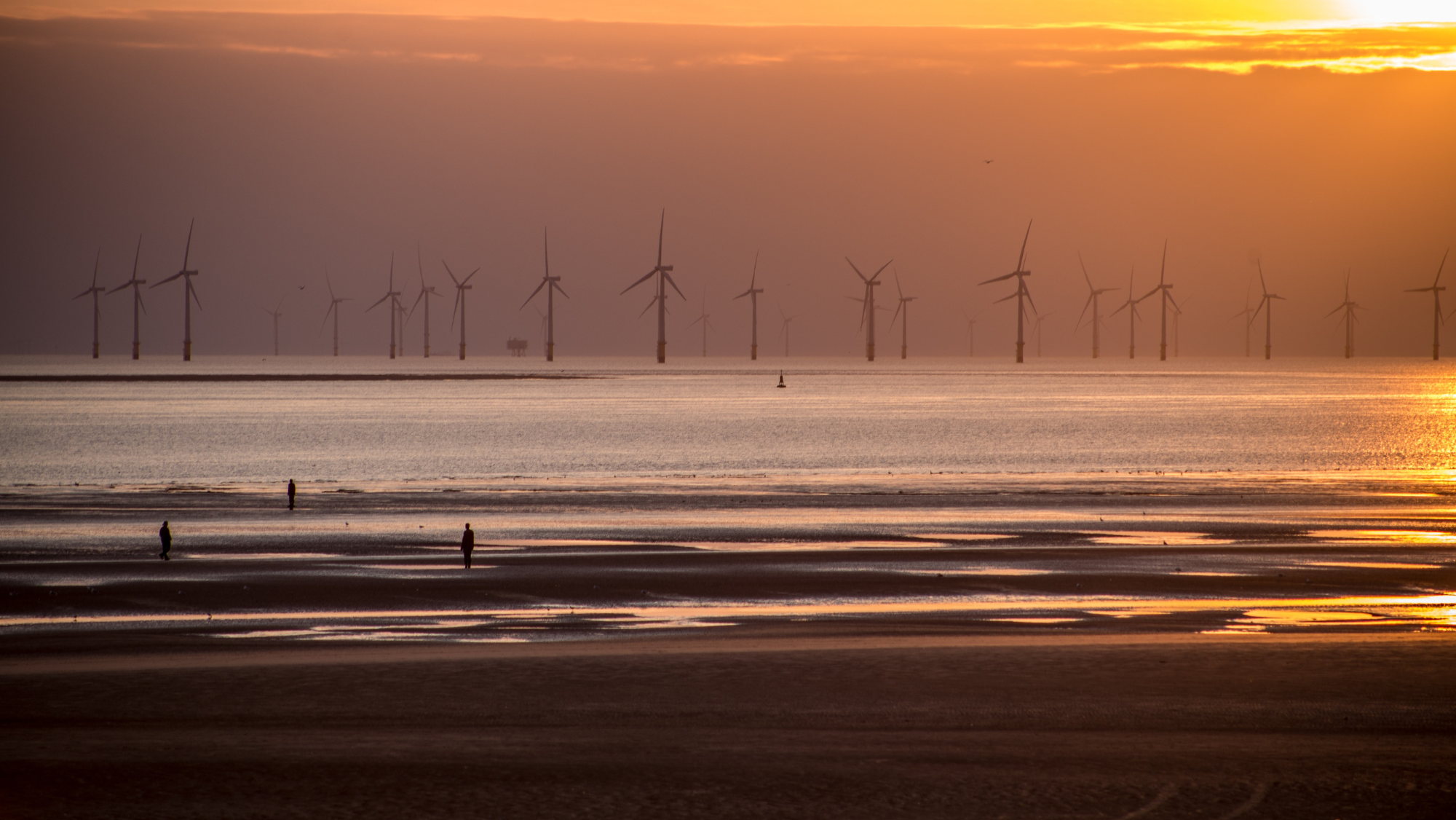 Imagen de varios aerogeneradores en una costa cercana a una playa. / Foto de Carl Raw en Unsplash