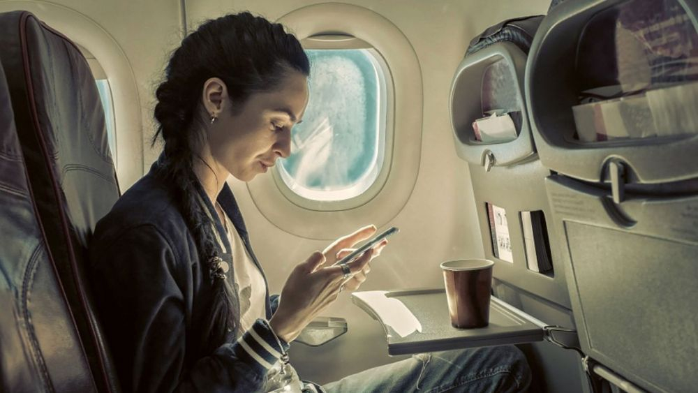 Una mujer utiliza un teléfono en un avión./ 