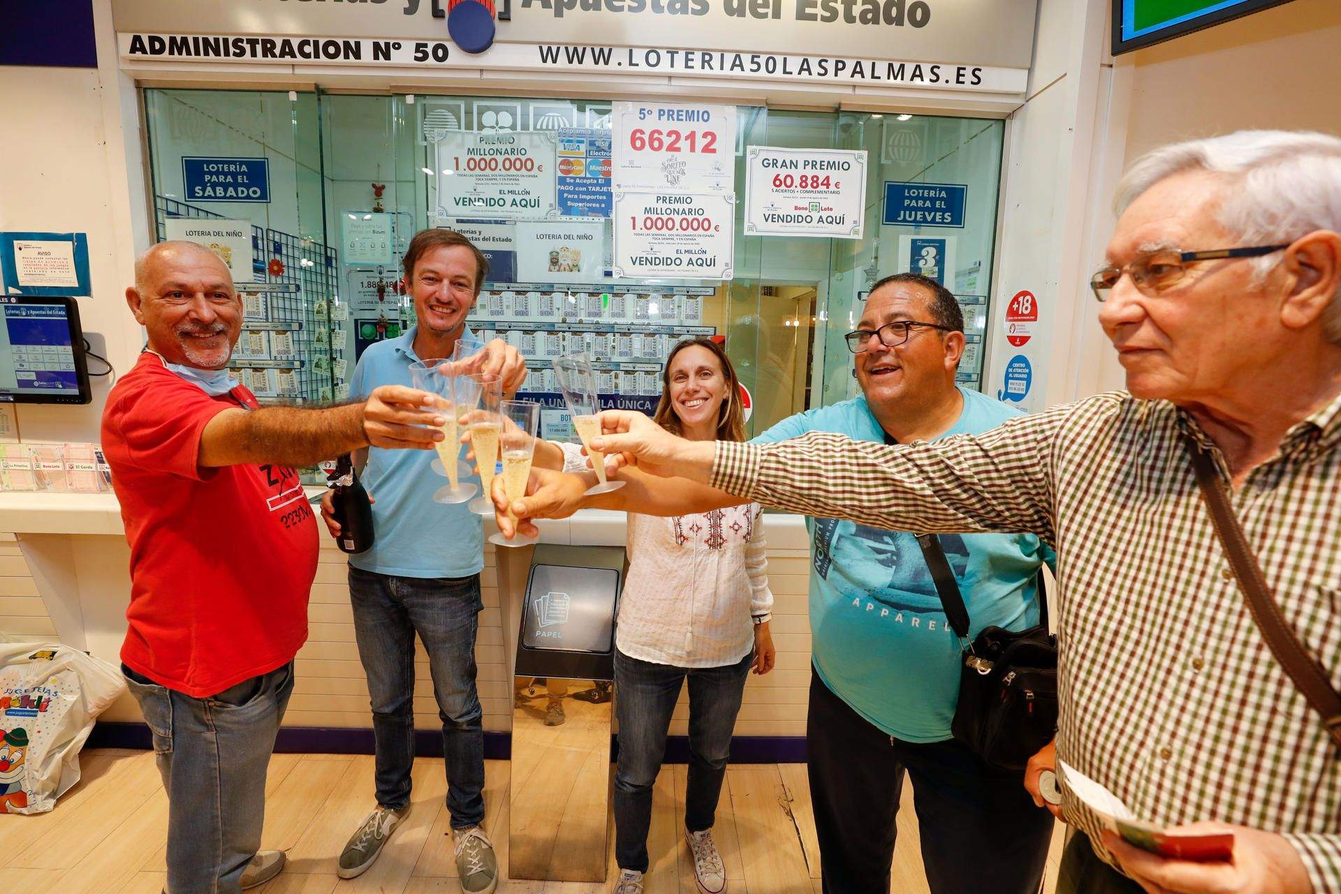 Los propietarios de la administración brindan con algunos de sus clientes habituales para celebrar que han vendido diez décimos 25.296, agraciado con un quinto premio de la Lotería de Navidad. / EFE/ Elvira Urquijo A.