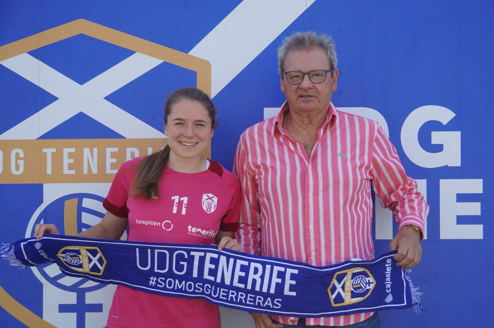 Aleksandra Zaremba y Sergio Batista sostienen la bufanda de la UD Granadilla frente al mural con el escudo del club en La Palmera./ UD GRANADILLA TENERIFE.
