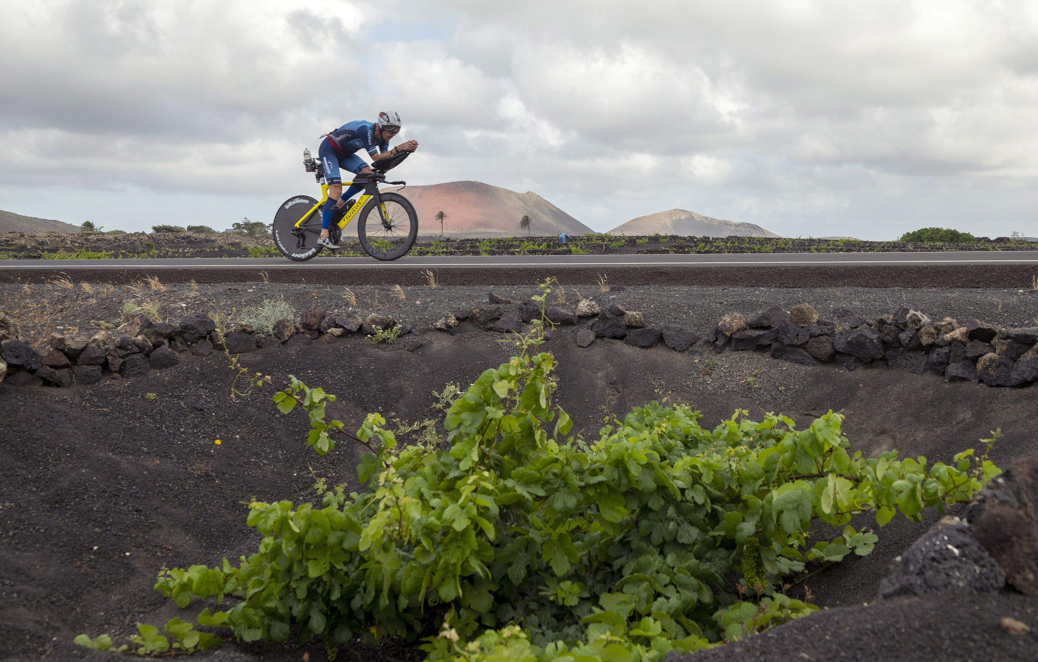 Un triatleta atraviesa un viñedo en los paisajes volcánicos, en la localidad de Masdache, durante el segmento de ciclismo del Ironman de Lanzarote 2023. / ADRIEL PERDOMO-EFE