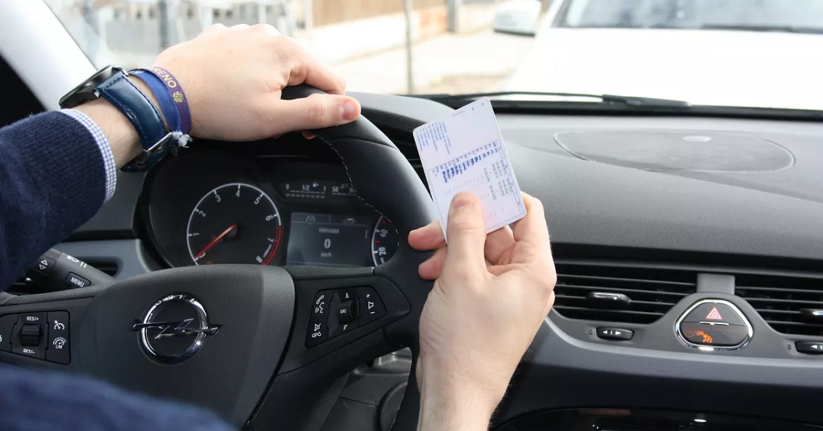 Un hombre con su carné de conducir en la mano mientras conduce su coche./ PIXABAY