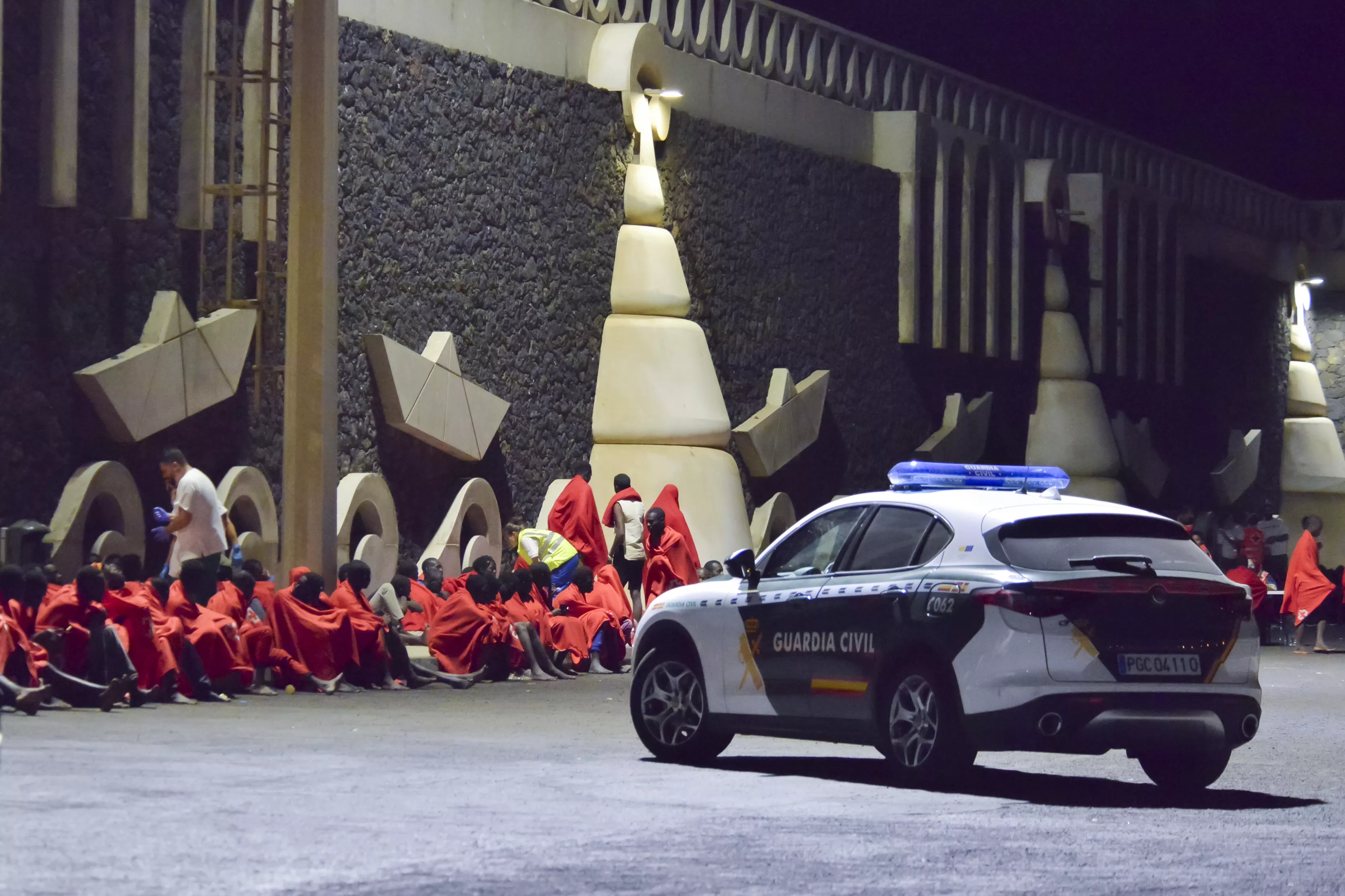 Un coche de la Guardia Civil vigila a un grupo de migrantes rescatados en la costa de El Hierro. / ALBERTO VALDÉS-EFE