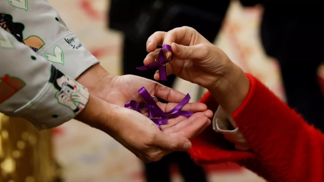 Una mujer le entrega a otra lazos violetas / EFE