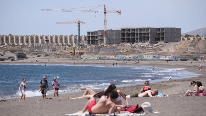 Turistas disfrutan del mar y el sol frente a las obras de construcción de un hotel en la playa de La Tejita, en el sur de Tenerife (Canarias). / ALBERTO VALDÉS-EFE