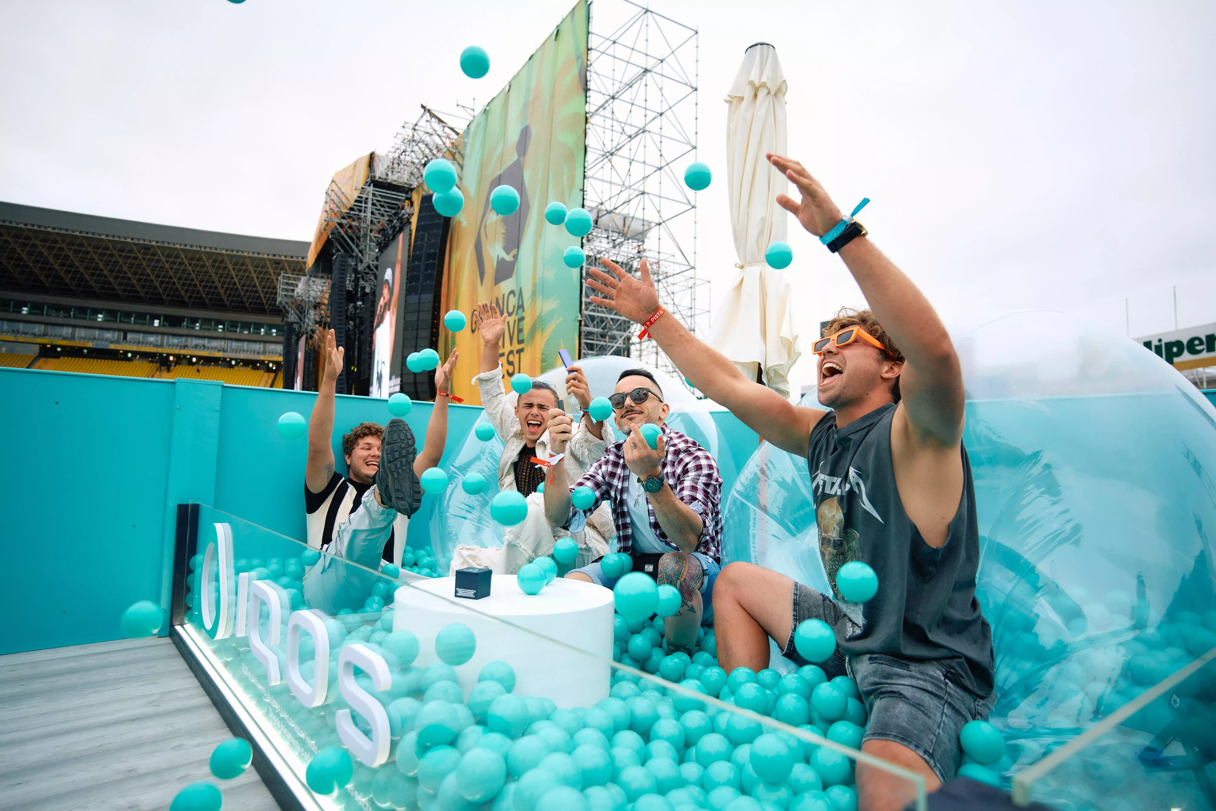 Cuatro usuarios disfrutan del espacio IQOS, que  inmerso en el característico azul turquesa de la marca y simulando un bar piscina como símbolo del disfrute, en el Granca Live Fest. / AH 