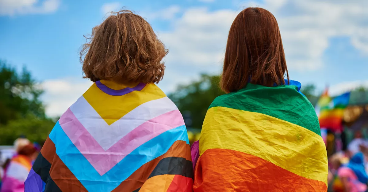 Imagen de dos personas con banderas del colectivo LGTBIQ+ / AH