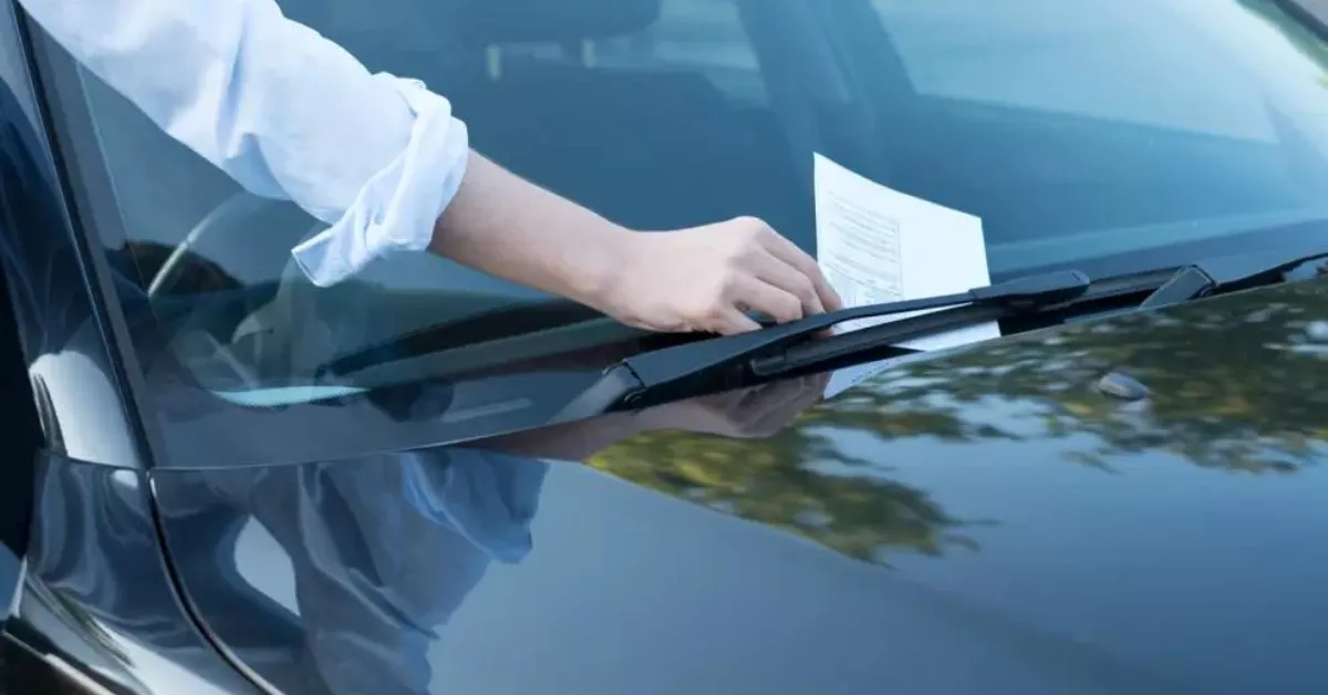 Una persona recoge una multa colocada en el parabrisas de su vehículo./ ARCHIVO