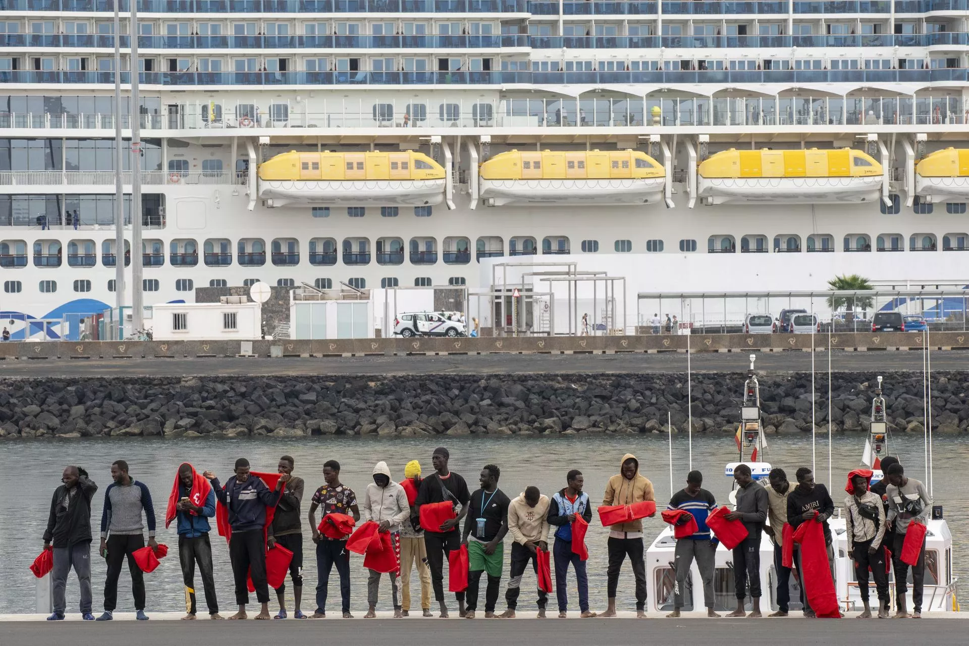 Un grupo de migrantes, tras ser rescatados en el mar, espera delante de un crucero en Arrecife. / ADRIEL PERDOMO-EFE