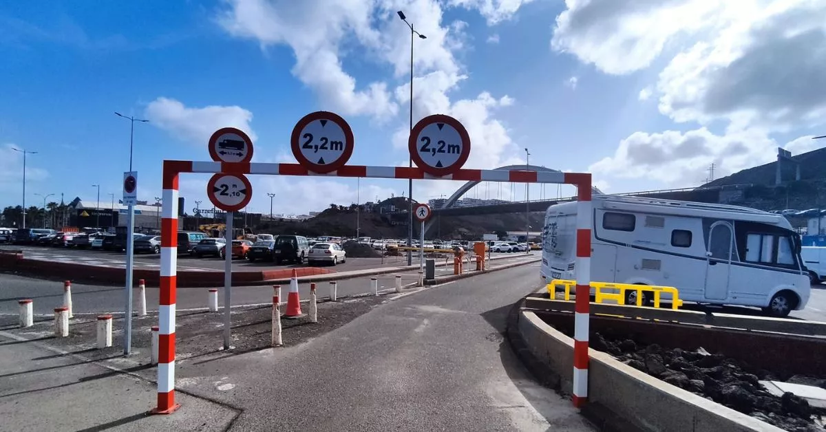 Nueva estructura de metal que impide la entrada de vehículos con más de 2,2 metros de altura al aparcamiento de El Rincón, como la autocaravana estacionada a la derecha, que entró antes de que se colocase la barrera. / AH
