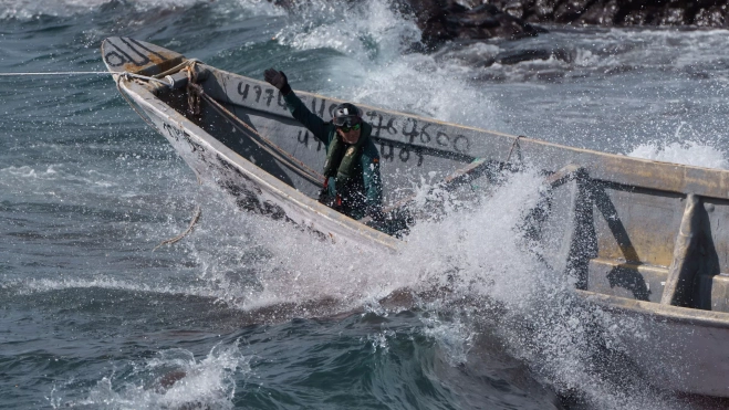 En la imagen, un agente de la Guardia Civil en el cayuco mientras lo sacan de la playa donde había varado. EFE/ Ramón De La Rocha