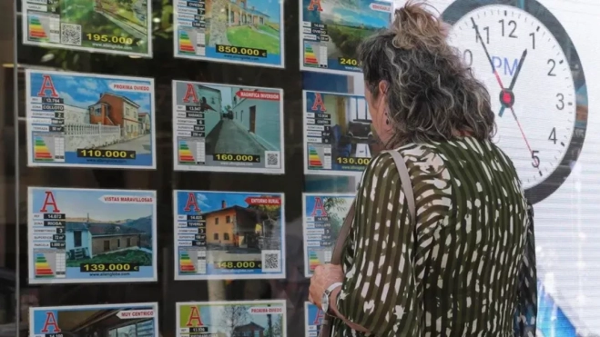 Una mujer mira el escaparate de una inmobiliaria con precios de viviendas / EFE
