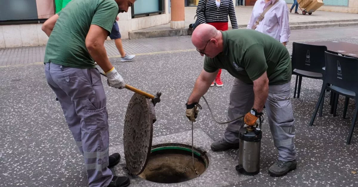 Dos trabajadores levantan una alcantarilla en la calle Ruiz de Alda para aplicar biocidas contra las plagas. / AH