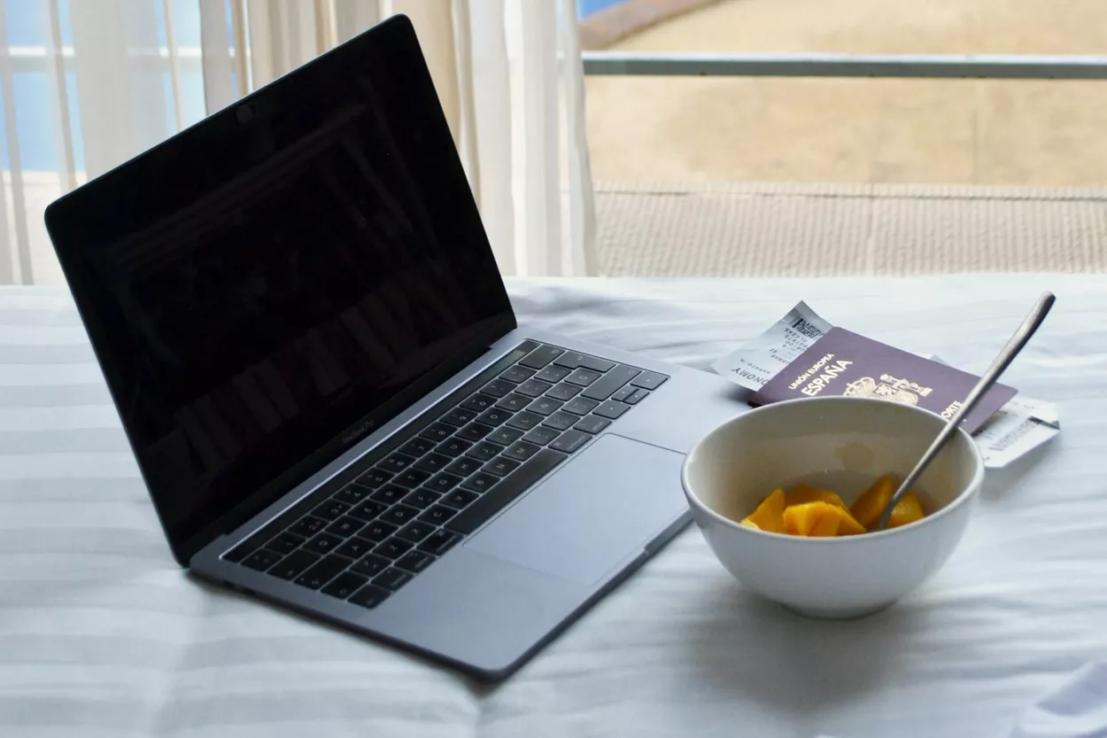 Pasaporte junto a un portátil y un bol de desayuno / UNSPLASH