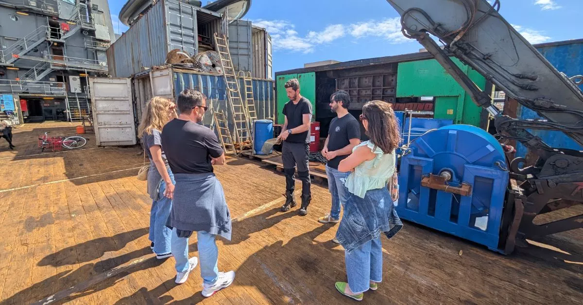 Miguel Moreno, con el casquete de un proyectil en las manos, explica lo que hacen en el 'N35' a un grupo de visitantes al buque. / AH