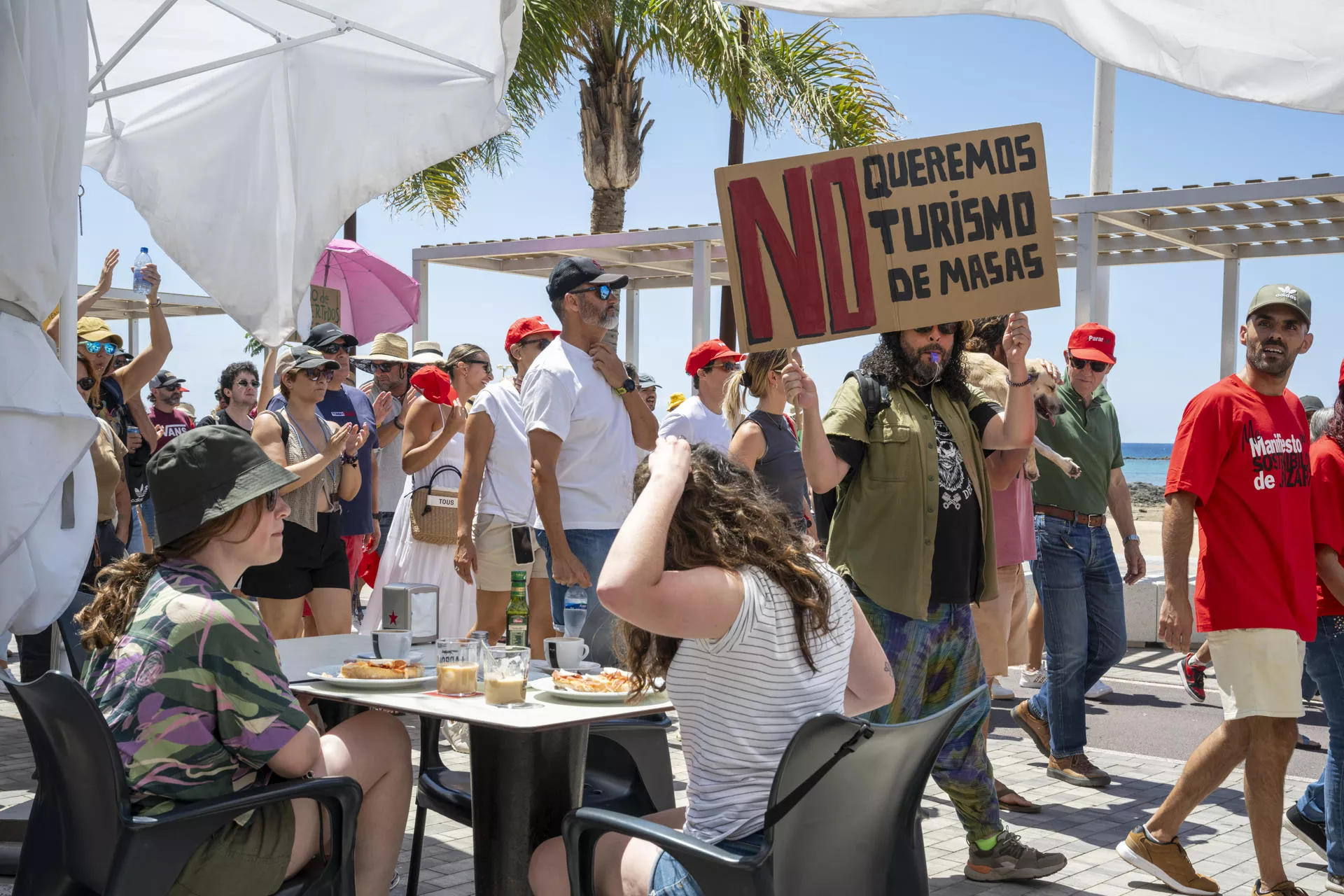 Turistas en una terraza ven pasar unas de las marchas de protesta de este fin de semana. / ADRIEL PERDOMO-EFE
