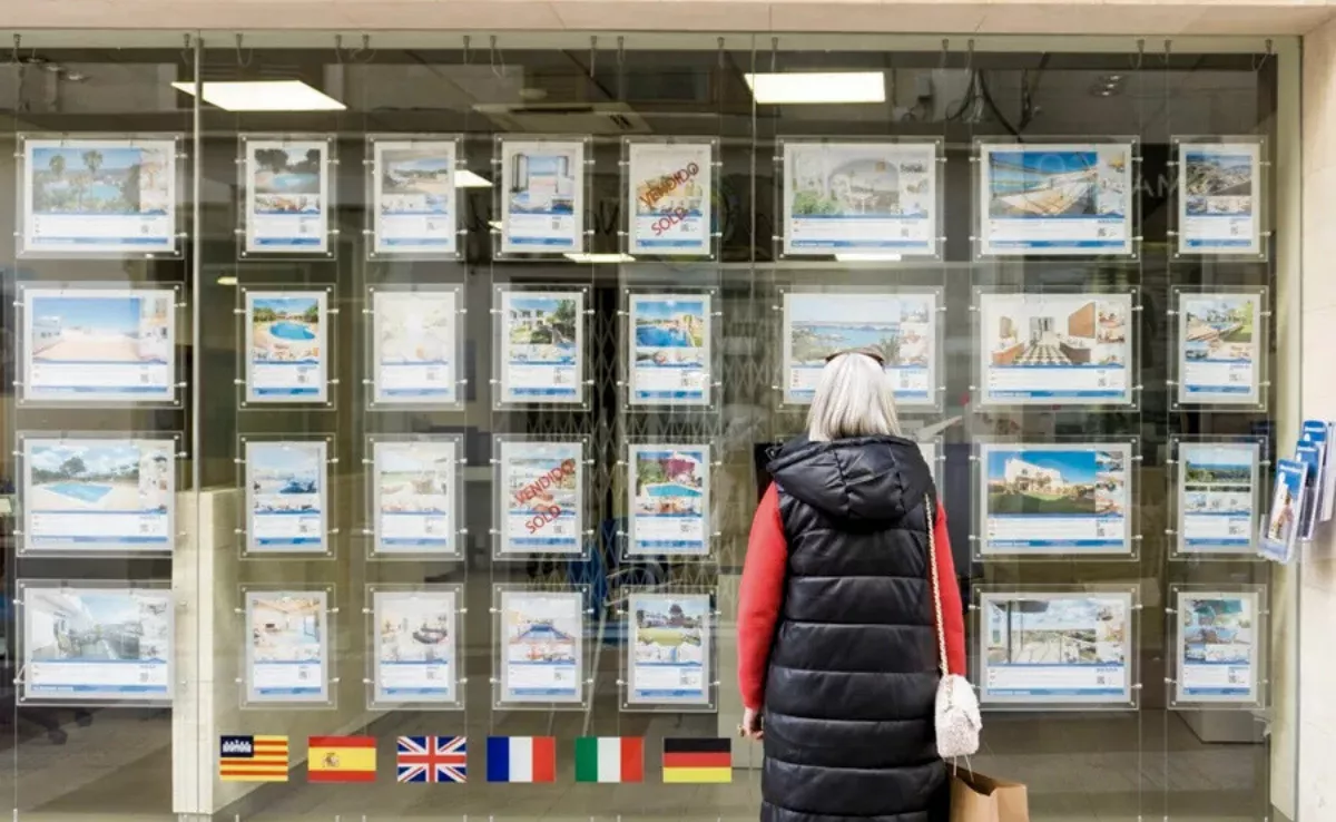 Una mujer mira las viviendas en venta ofertadas en el escaparate de una inmobiliaria / EFE