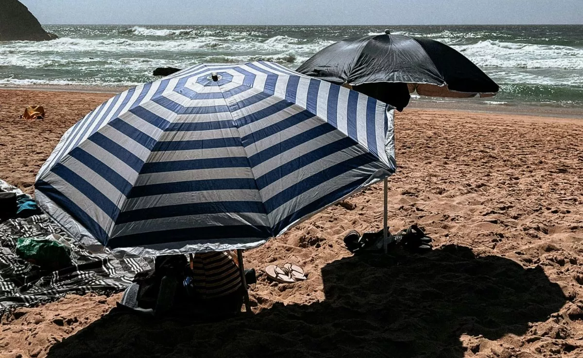 Personas bajo una sombrilla en la playa. /Pexels