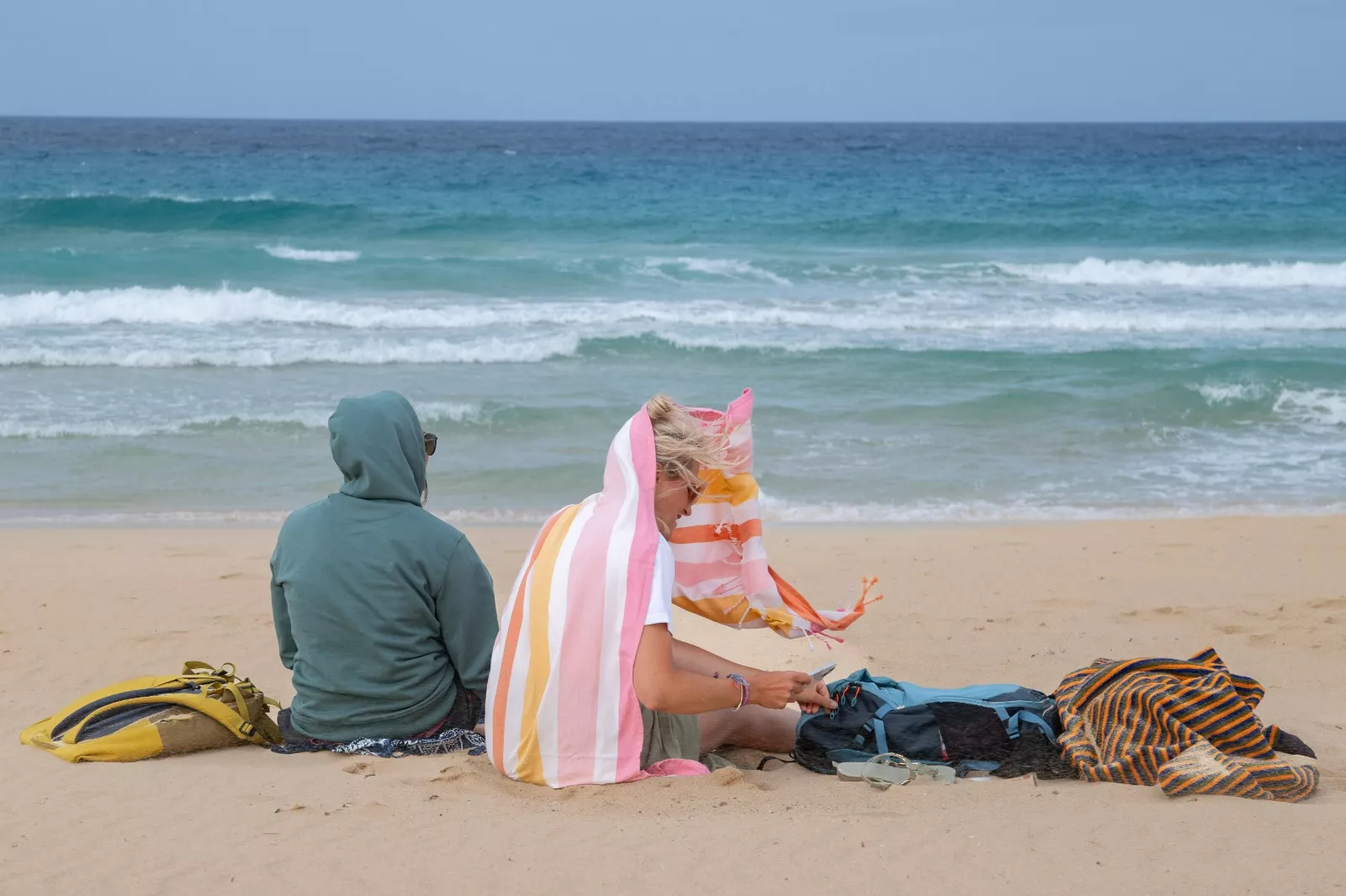 Dos personas se cubren del viento este domingo, en las playas de Corralejo, en el municipio de La Oliva (Fuerteventura). / CARLOS DE SÁA-EFE