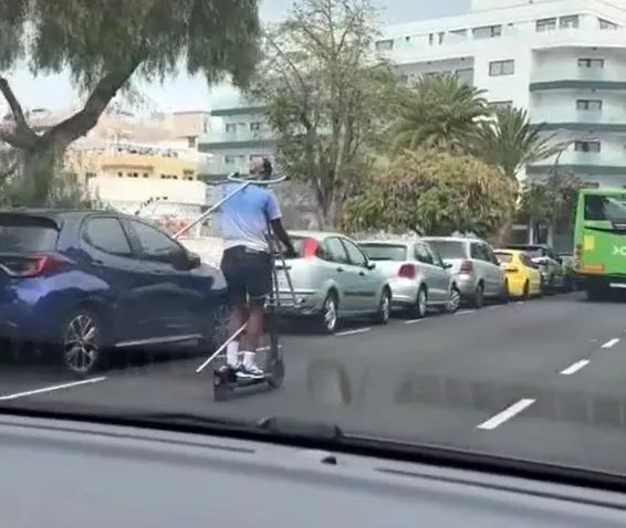 Una mujer conduce un patinete por el Puerto de la Cruz llevando un perchero a cuestas. / AYUNTAMIENTO DE PUERTO DE LA CRUZ