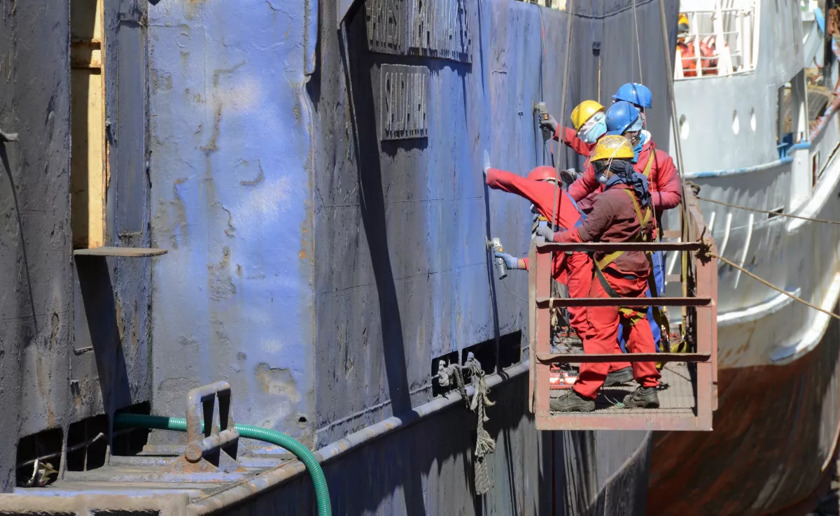 Trabajadores pintando un barco. / CANVA