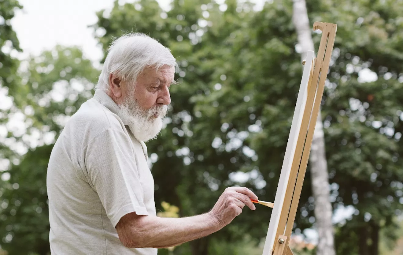 Hombre mayor pintando al aire libre sobre un lienzo