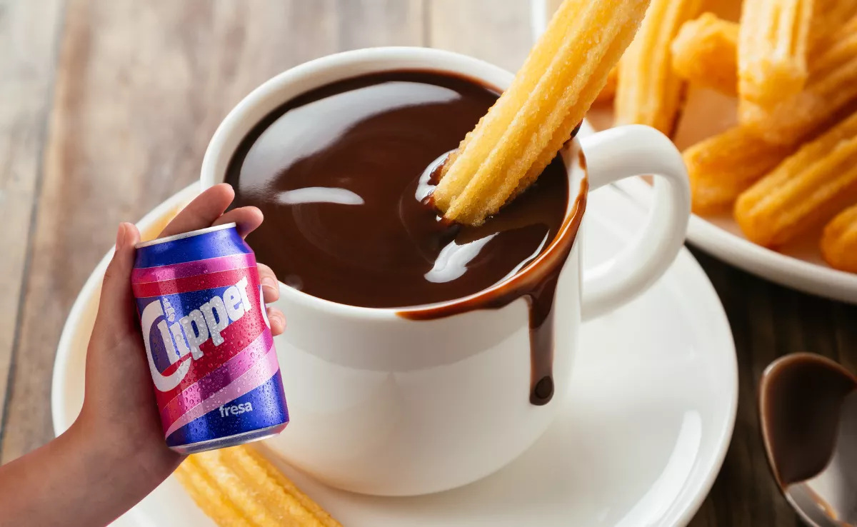 Imagen de unos churros con chocolate y una lata de Clipper / AH