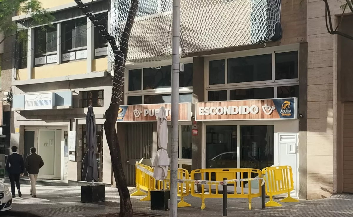 Dos personas caminan frente a la cafetería Puerto Escondido, en la calle homónima, que permanece cerrada por la caída de cascotes./ AH