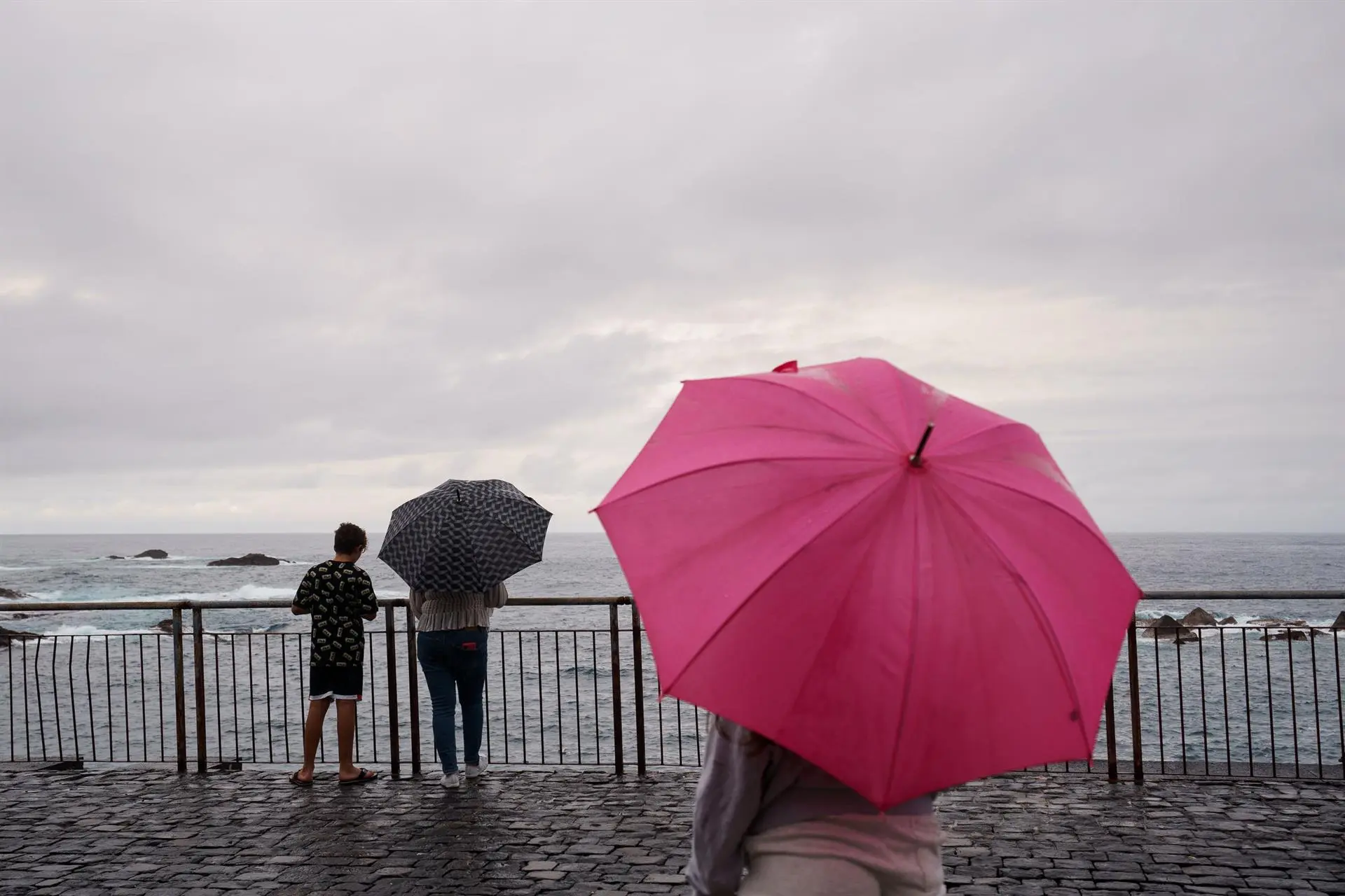 Unas personas contemplan el mar en la costa del municipio de Garachico, en el norte de Tenerife, en un día de frío y lluvias. / EFE - RAMÓN DE LA ROCHA