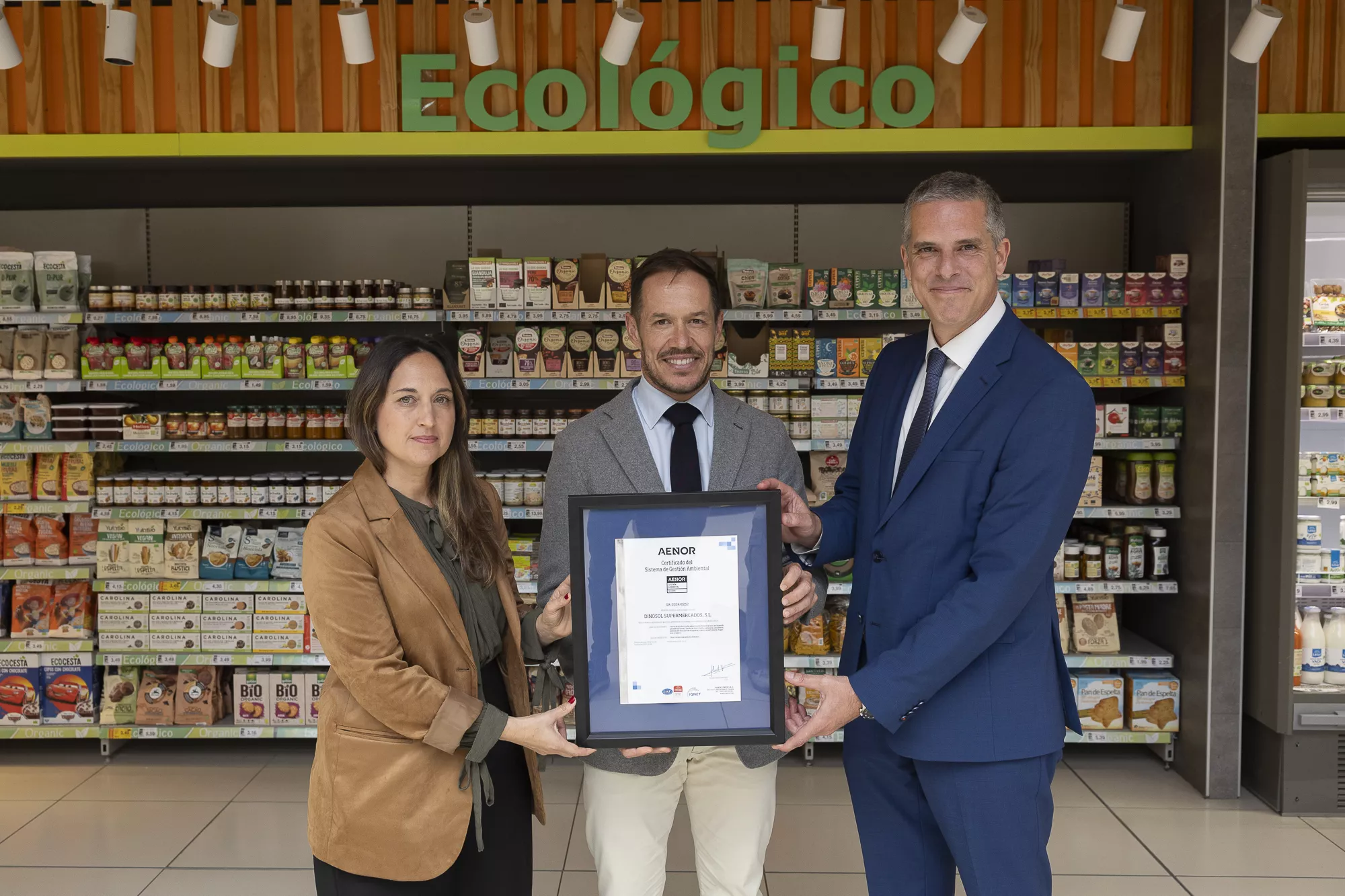 Gara Sánchez (HiperDino), Mariano Hernández Zapata (Gobierno de Canarias) y Javier Lantigua (AENOR) muestran el certificado ISO 14001 que avala la gestión sostenible de la cadena.