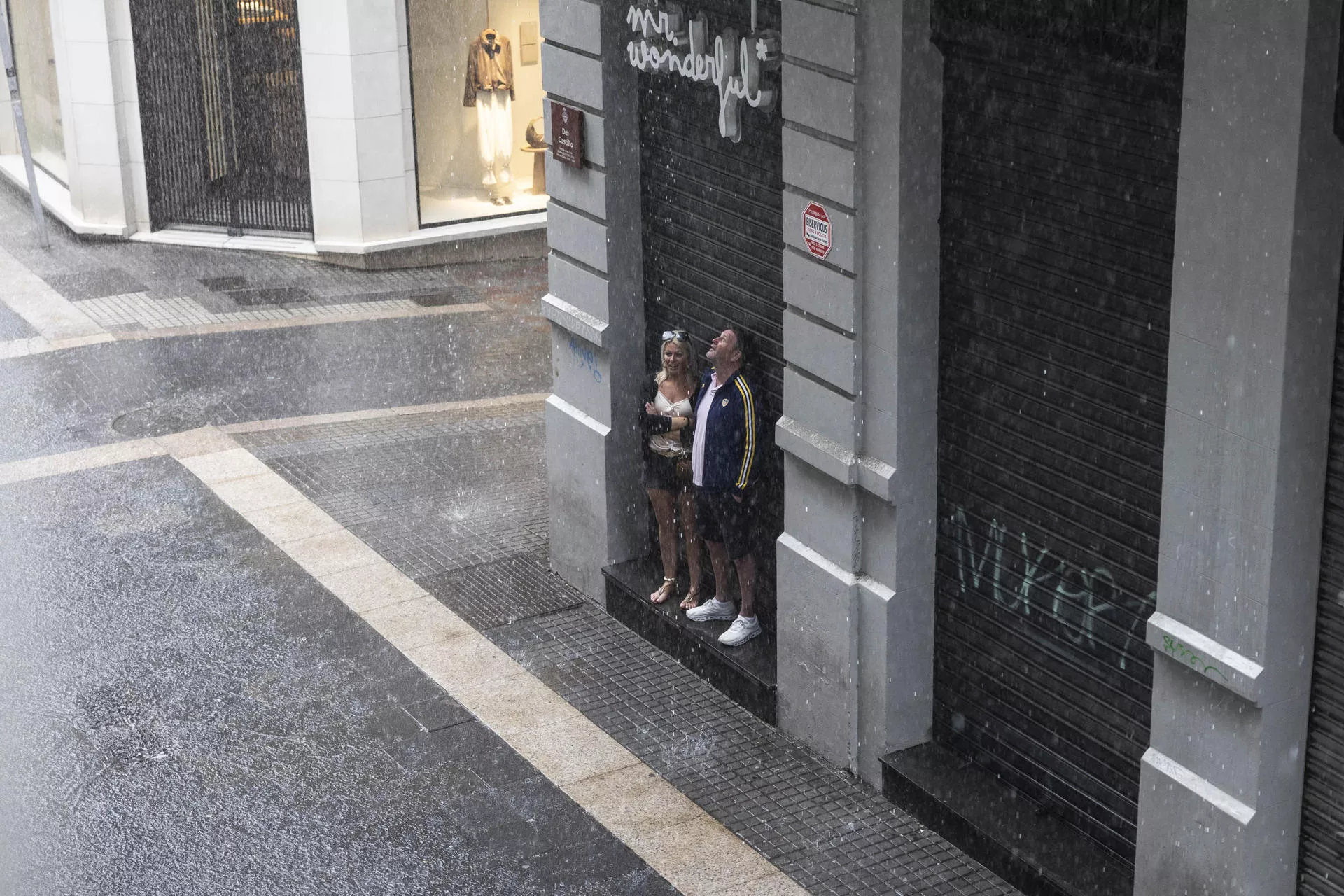 Una pareja se resguarda en la puerta de una tienda de la lluvia caída en una zona comercial de la capital tinerfeña. / EFE - MIGUEL BARRETO