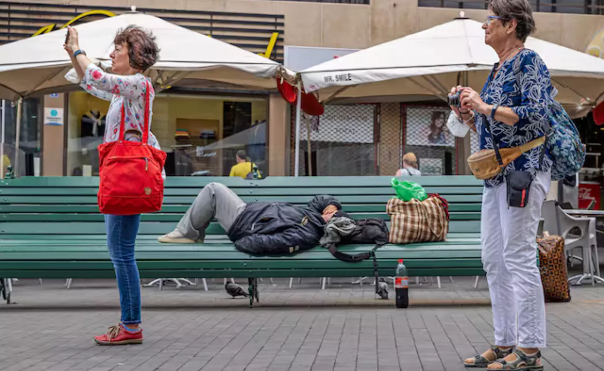 Turistas en Santa Cruz de Tenerife mientras una persona en posible situación de sinhogarismo está recostada en un banco / GETTYI MAGES