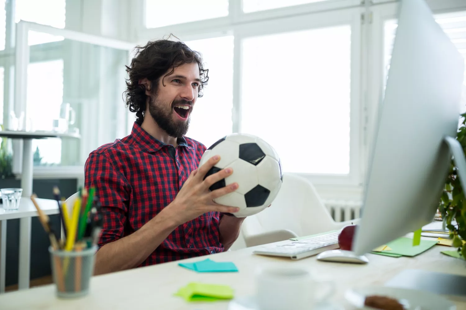 Hombre sonriente con un balón de fútbol frente a un ordenador